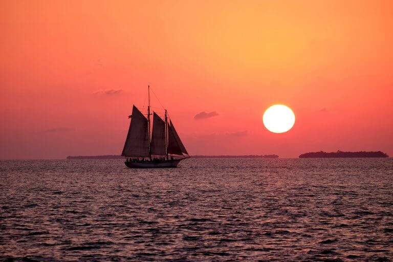 Voilier prière pour la France, en mer au crépuscule, soleil au-dessus de l’horizon, et îles en vue sur l’horizon