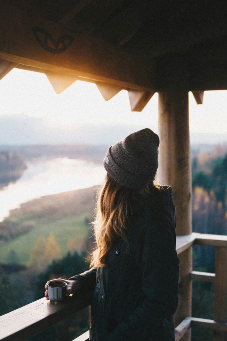 Jeune-femme dans un mirador en pleine nature regardant un lac entouré de forêt un mug prière pour la France à la main